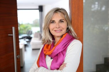 Cheerful senior woman standing at home entrance door